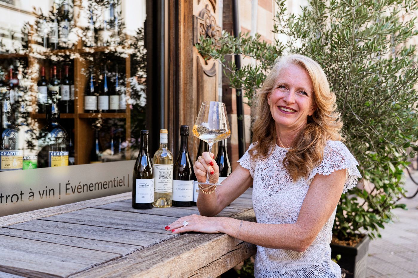 Isabelle Kraemer, un verre de vin blanc à la main, attablée en terrasse devant la cave